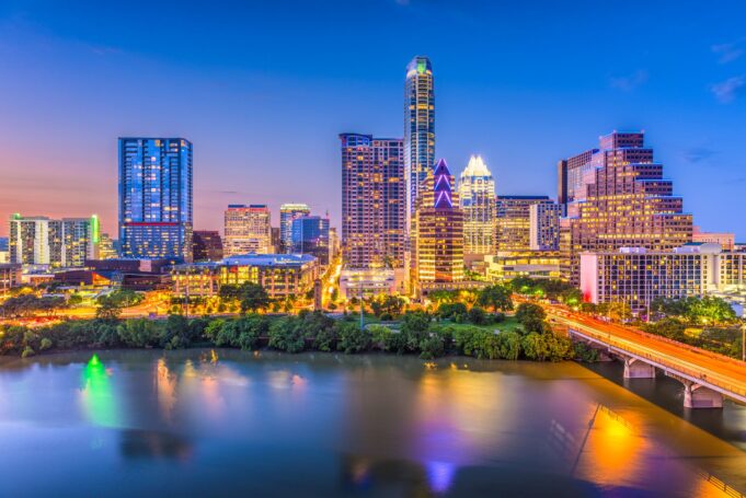 The vibrant cityscape of Austin, Texas, illuminated at twilight, reflects beautifully on the calm waters of the river.