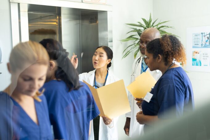 A diverse group of medical professionals engage in a discussion, reviewing patient files together in a hospital setting.