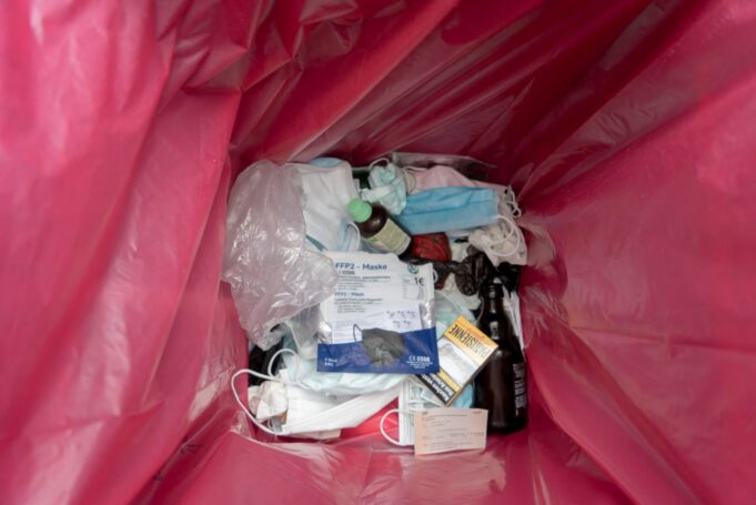 A pink trash bag filled with discarded medical masks, packaging, and various medical waste items.