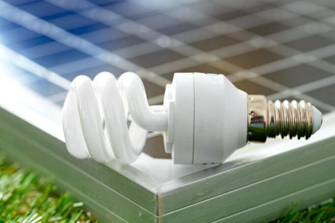 A close-up image of a compact fluorescent light bulb resting on a solar panel, symbolizing the integration of renewable energy and energy-efficient lighting.