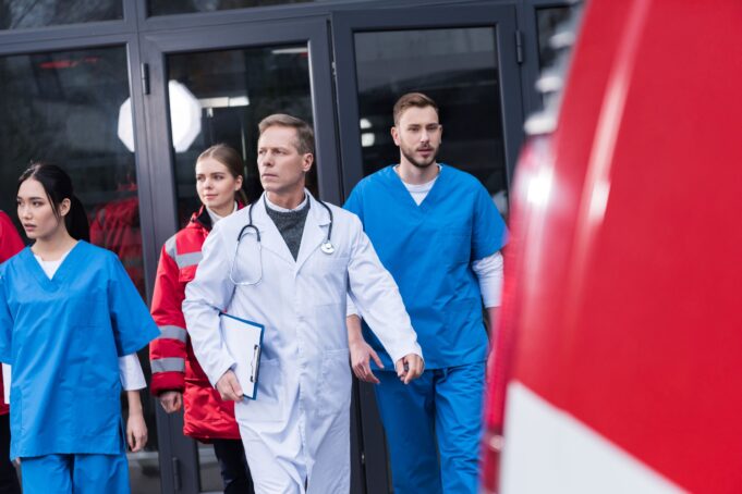 A team of healthcare professionals, including doctors and paramedics, urgently exits a hospital building.